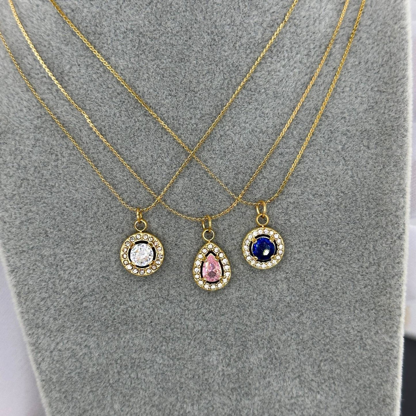 Three gold necklaces with different colored gemstones on a gray surface