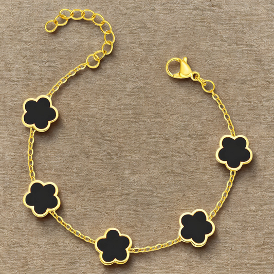 Gold bracelet with black clover-shaped charms on a beige background