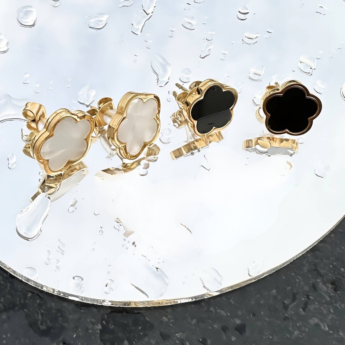 Gold and black clover-shaped earrings on a clear stand.