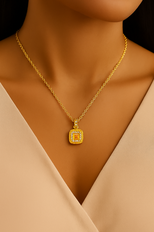 Gold necklace with a square pendant on a model wearing a beige top.