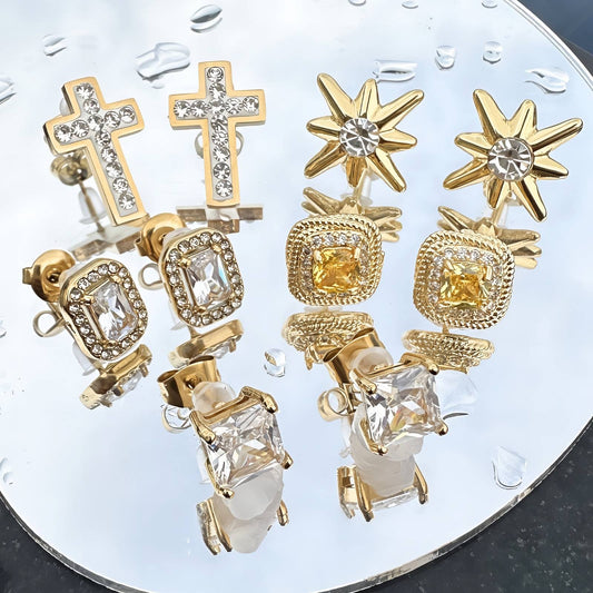 Set of gold earrings with various designs on a clear stand.