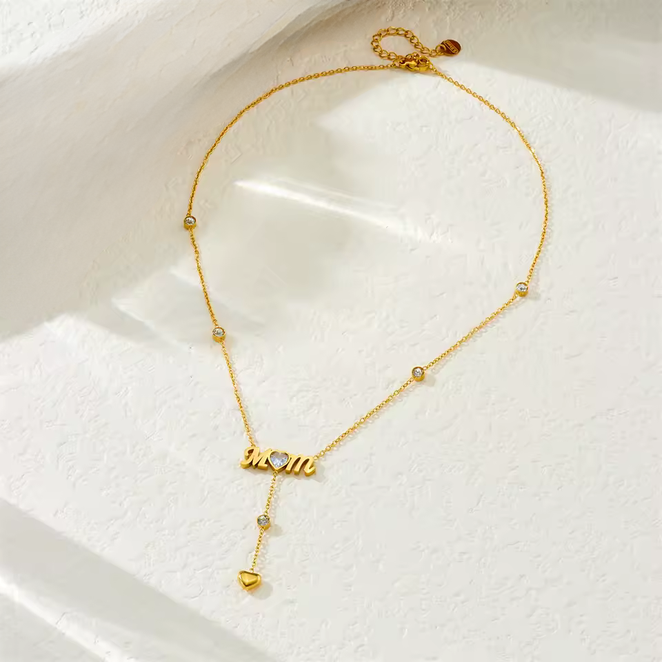 Gold necklace with 'mom' pendant on a white surface