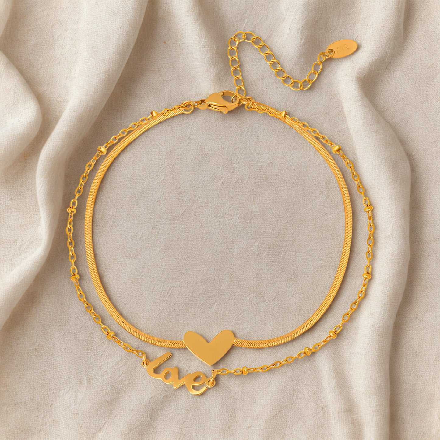 Gold bracelet with heart and 'love' charm on a beige fabric background