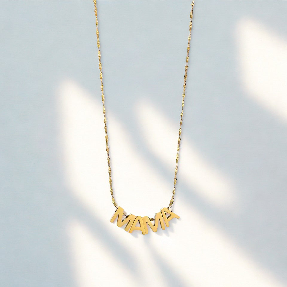 Gold necklace with 'MAMA' pendant on a light gray background