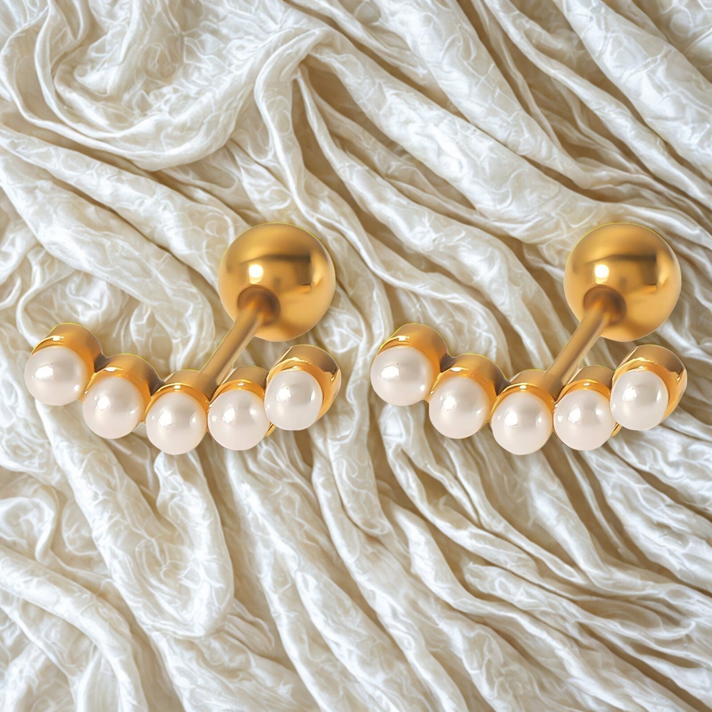 Pair of gold and pearl earrings on a textured white fabric background