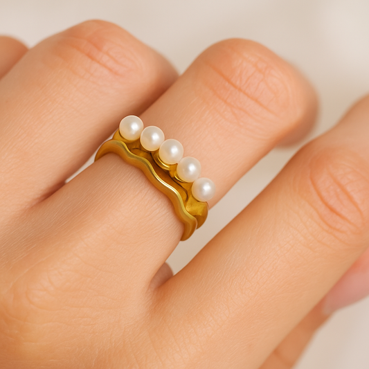 Gold ring with pearls on a finger against a neutral background