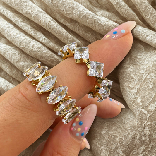 Gold and clear gemstone rings on a hand with beige fabric background