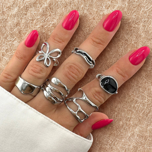 Hand wearing multiple silver rings with pink nail polish on a textured beige background