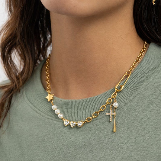 Gold devotion charm necklace with cross charm, heart details, pearls, and layered chain on white background