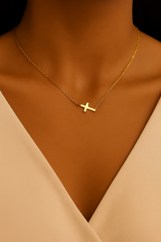 Gold necklace with a cross pendant on a model wearing a beige top.