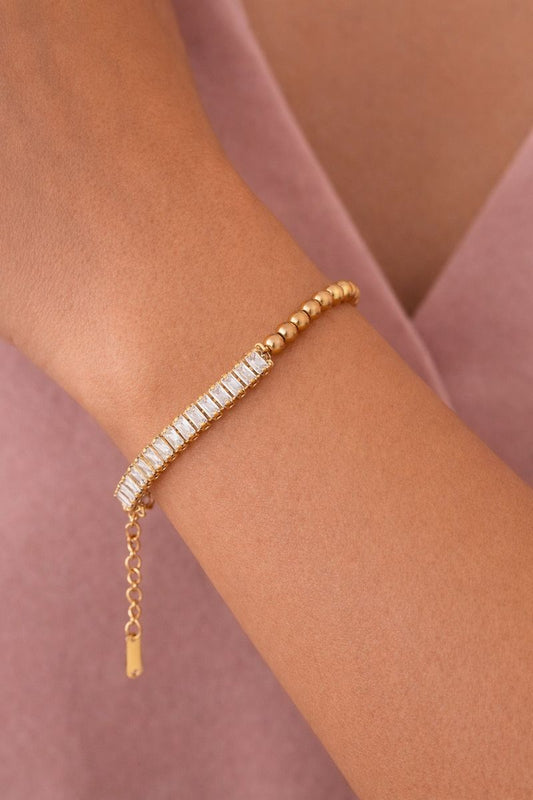Gold bracelet with a chain extension on a wrist against a pink fabric background