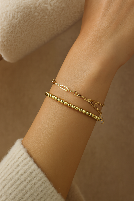 Gold bracelets on a wrist with a neutral background