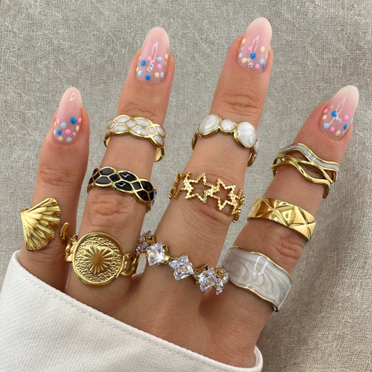 Hand wearing multiple gold rings on a neutral background