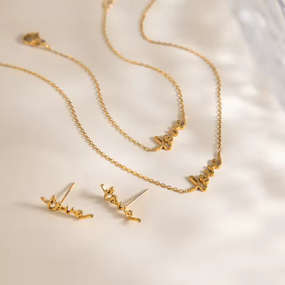 Gold 'love' necklace and earrings on a light background