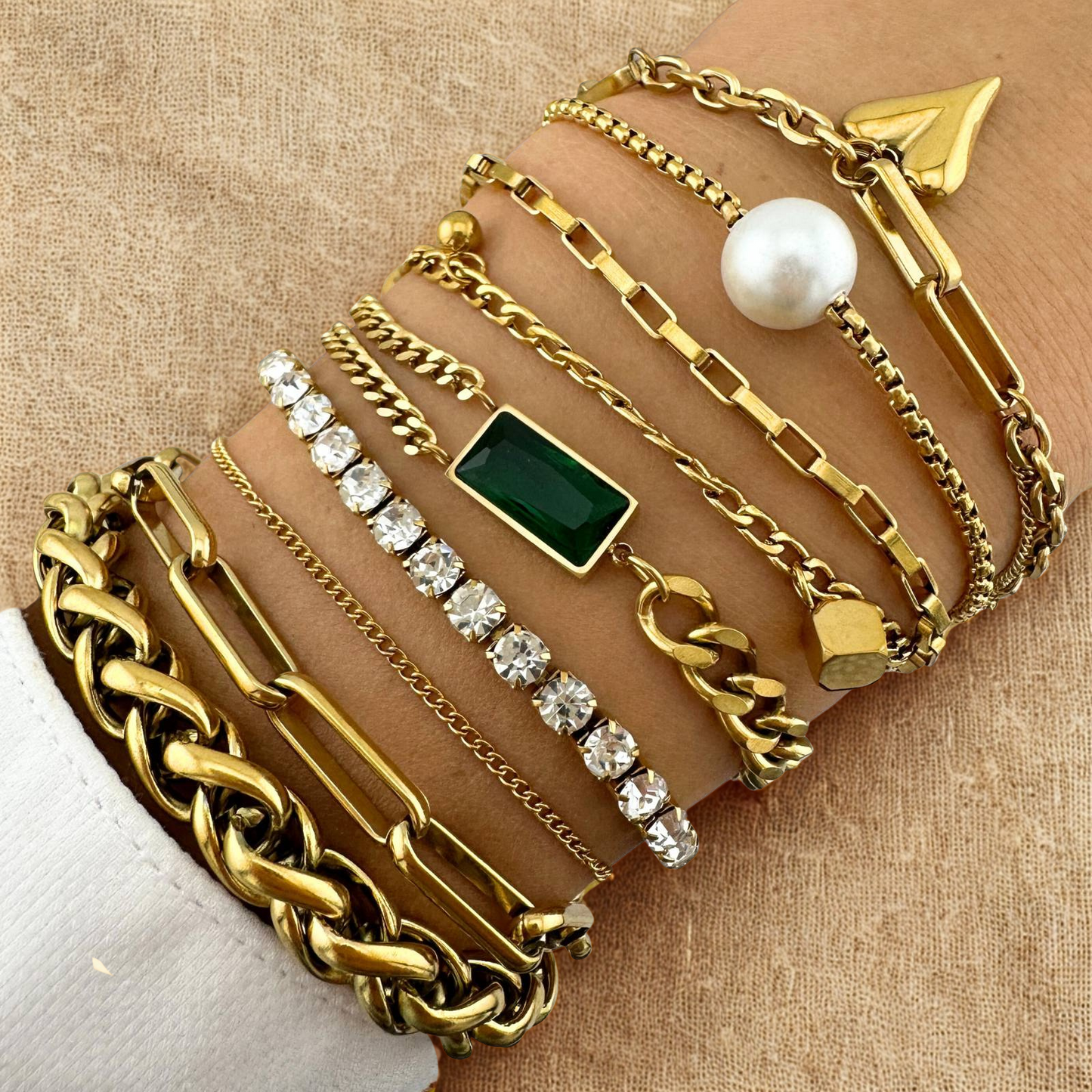 Multiple gold bracelets with various designs on a beige background
