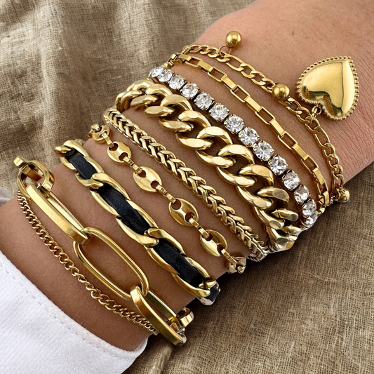 Multiple gold bracelets with different designs on a wrist against a beige fabric background