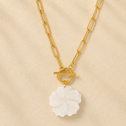 Gold chain necklace with a white floral pendant on a beige background