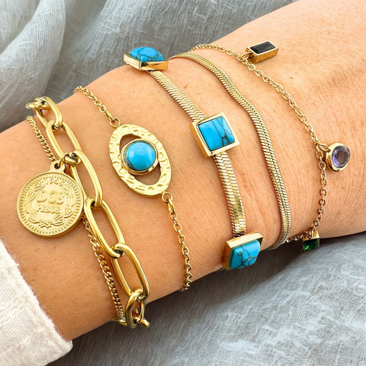 Gold bracelets with turquoise stones on a wrist against a gray fabric background