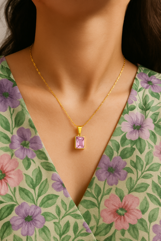 Gold necklace with a pink pendant worn by a model in a floral dress