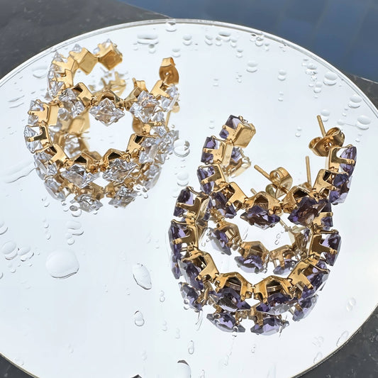 Gold and purple hoop earrings on a clear glass surface with water droplets.