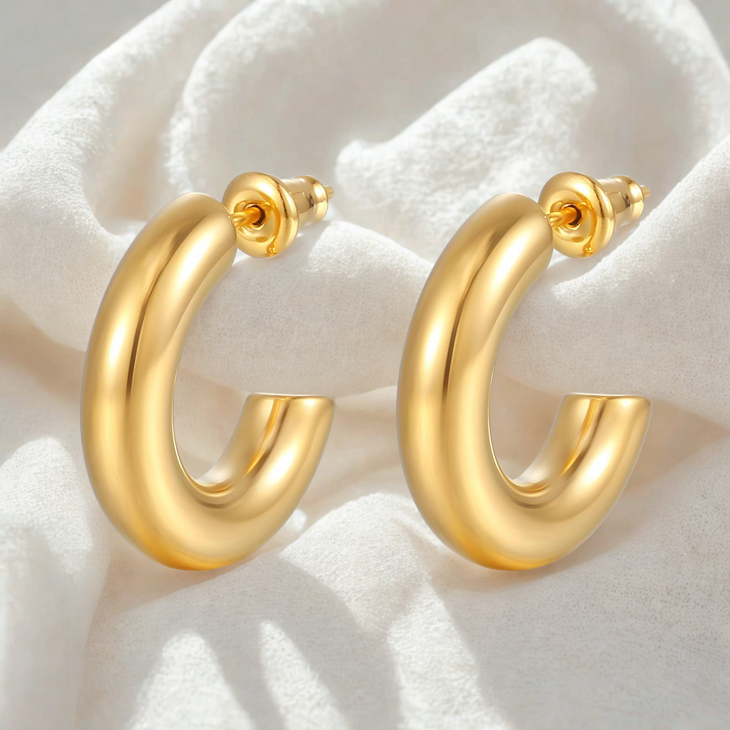Gold hoop earrings on a soft white fabric background