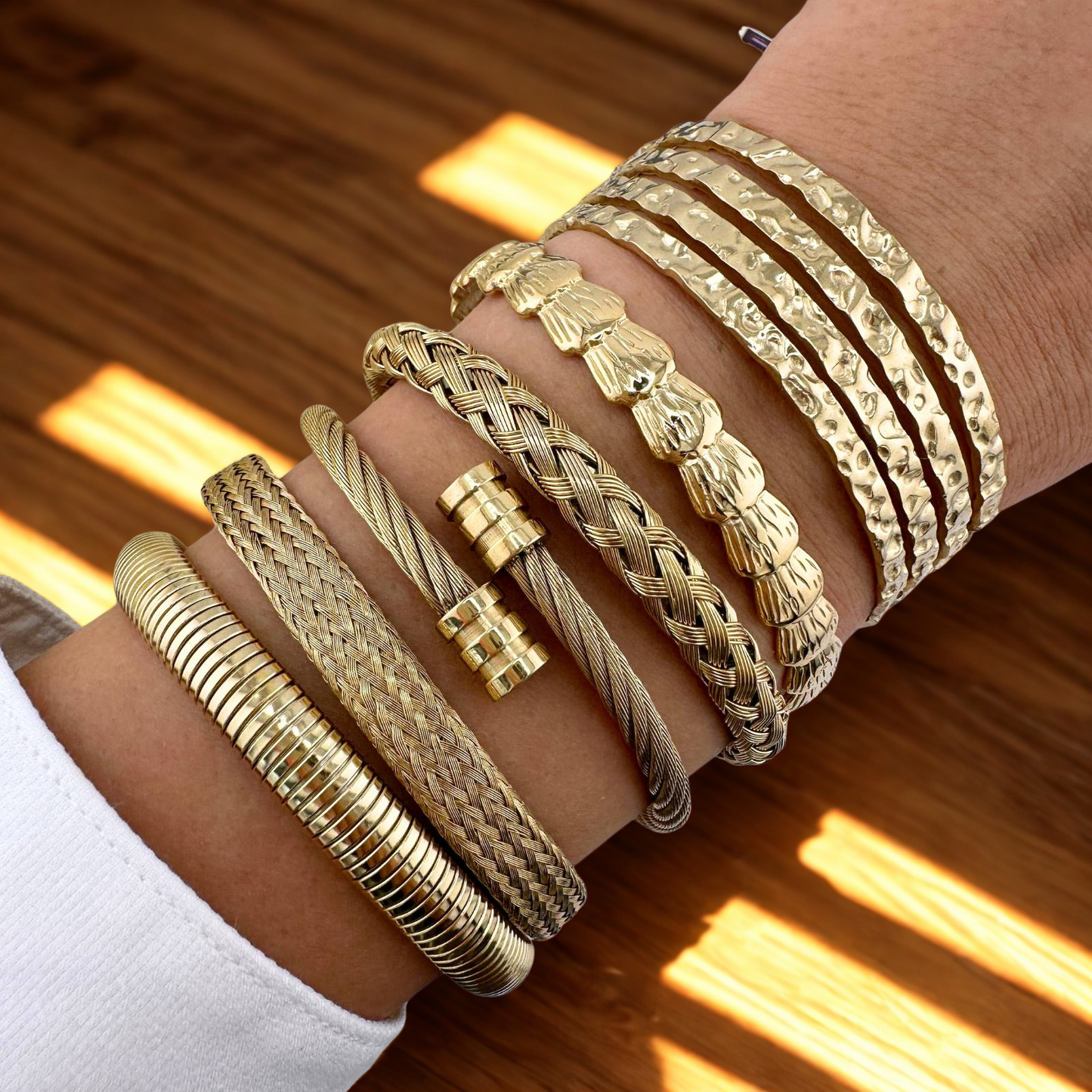 Gold bracelets on a wrist with a wooden background