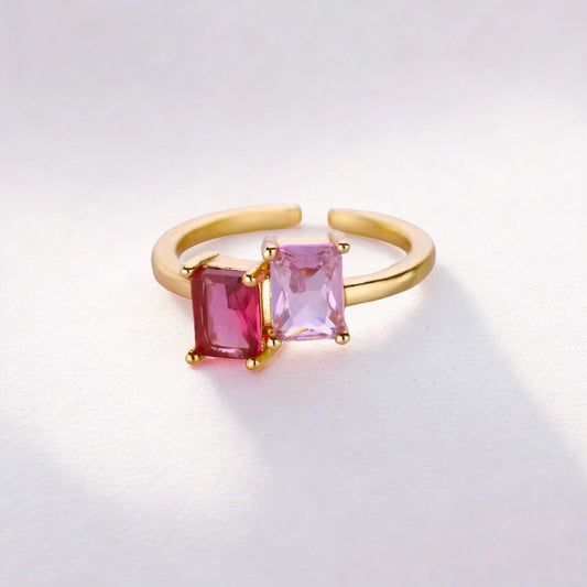 Gold ring with pink and red gemstones on a light gray background