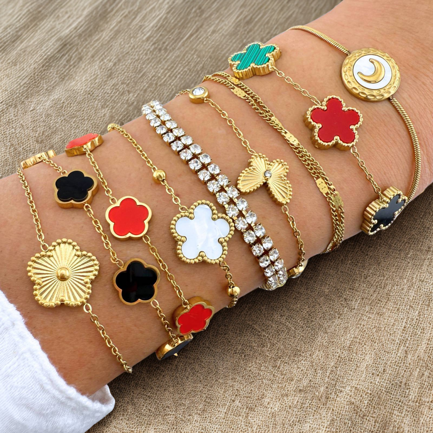 Multiple gold bracelets with colorful flower charms on a wrist against a wooden background