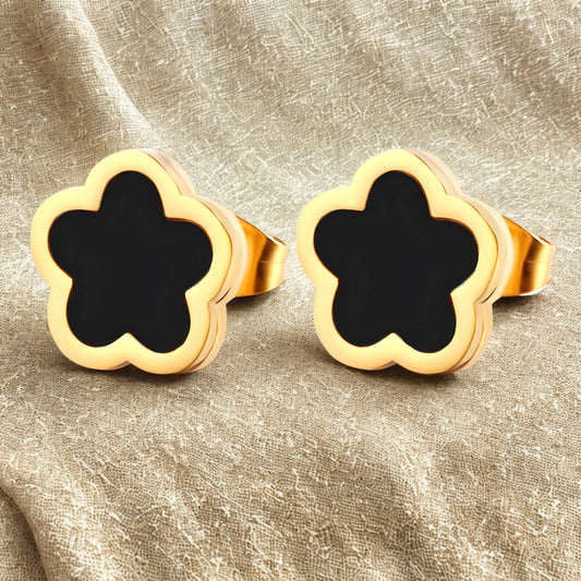Gold clover flower-shaped earrings with black centers on a beige fabric background