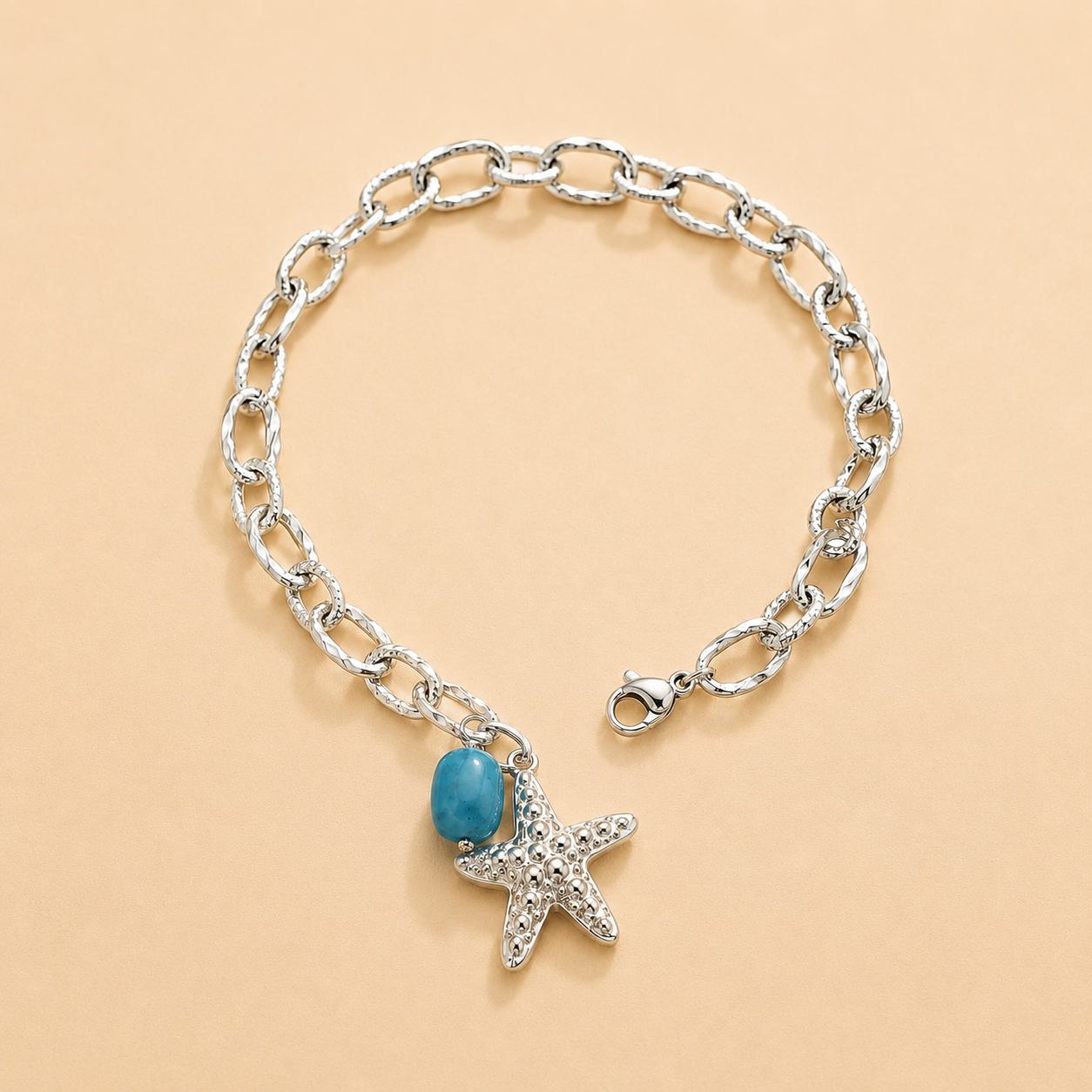 Silver chain bracelet with starfish and turquoise charm on a beige background