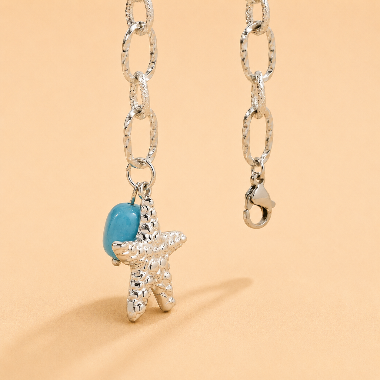 Silver chain necklace with a starfish and turquoise bead charm on a beige background