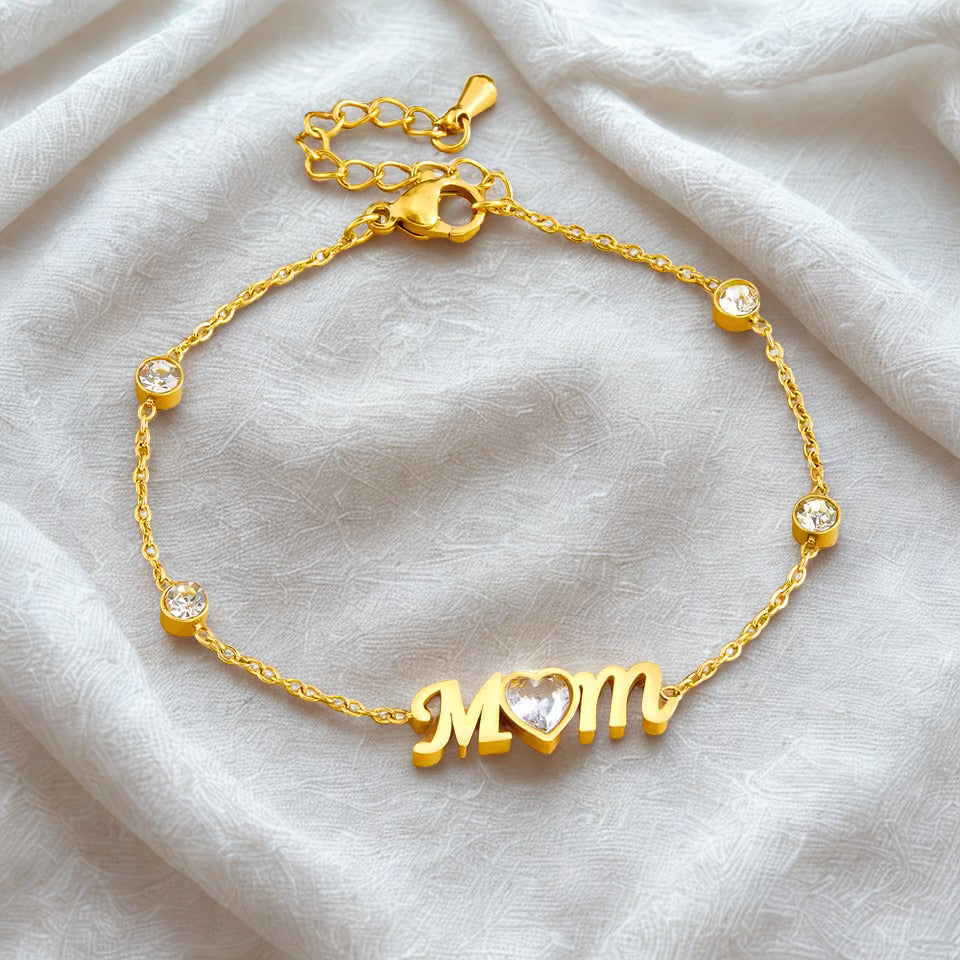 Gold bracelet with 'MOM' charm on a light fabric background