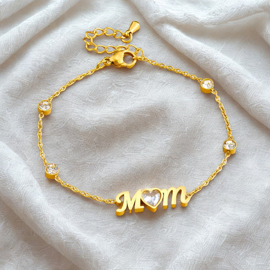Gold bracelet with 'MOM' charm on a light fabric background