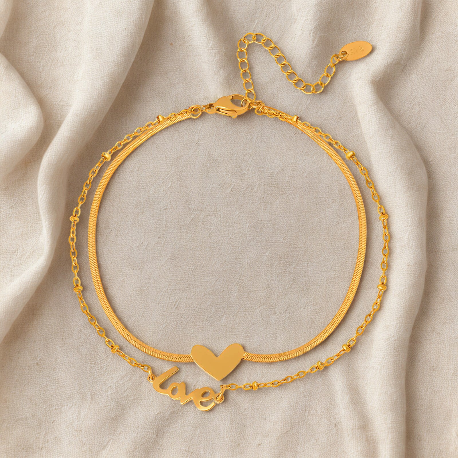 Gold bracelet with heart and 'love' charm on a beige fabric background