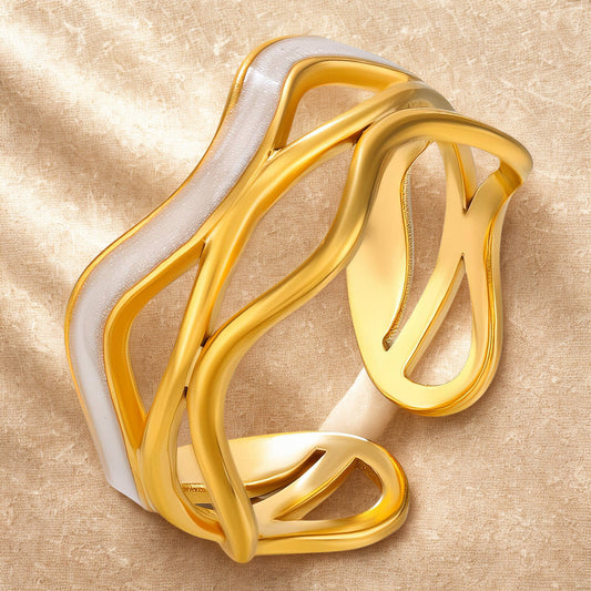 Gold and white ring on a beige textured background. Gold and white sculptural open band ring with flowing design – Breathe Ring by 31:10 Jewelry.