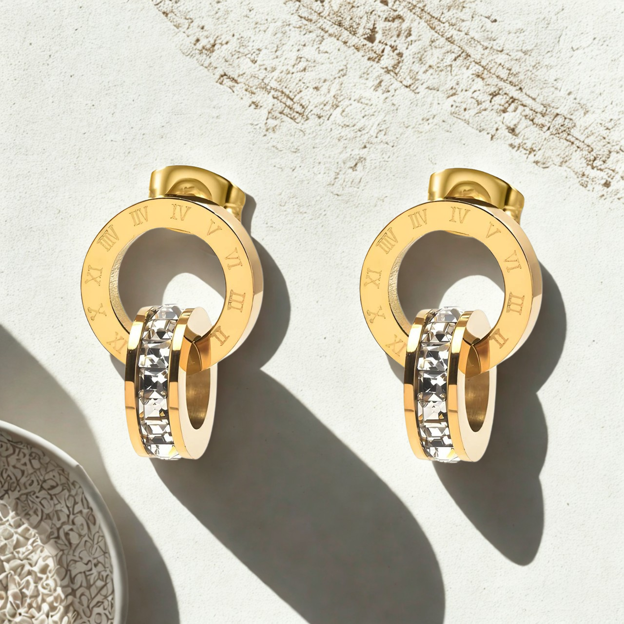 Gold hoop earrings with embedded stones on a textured surface