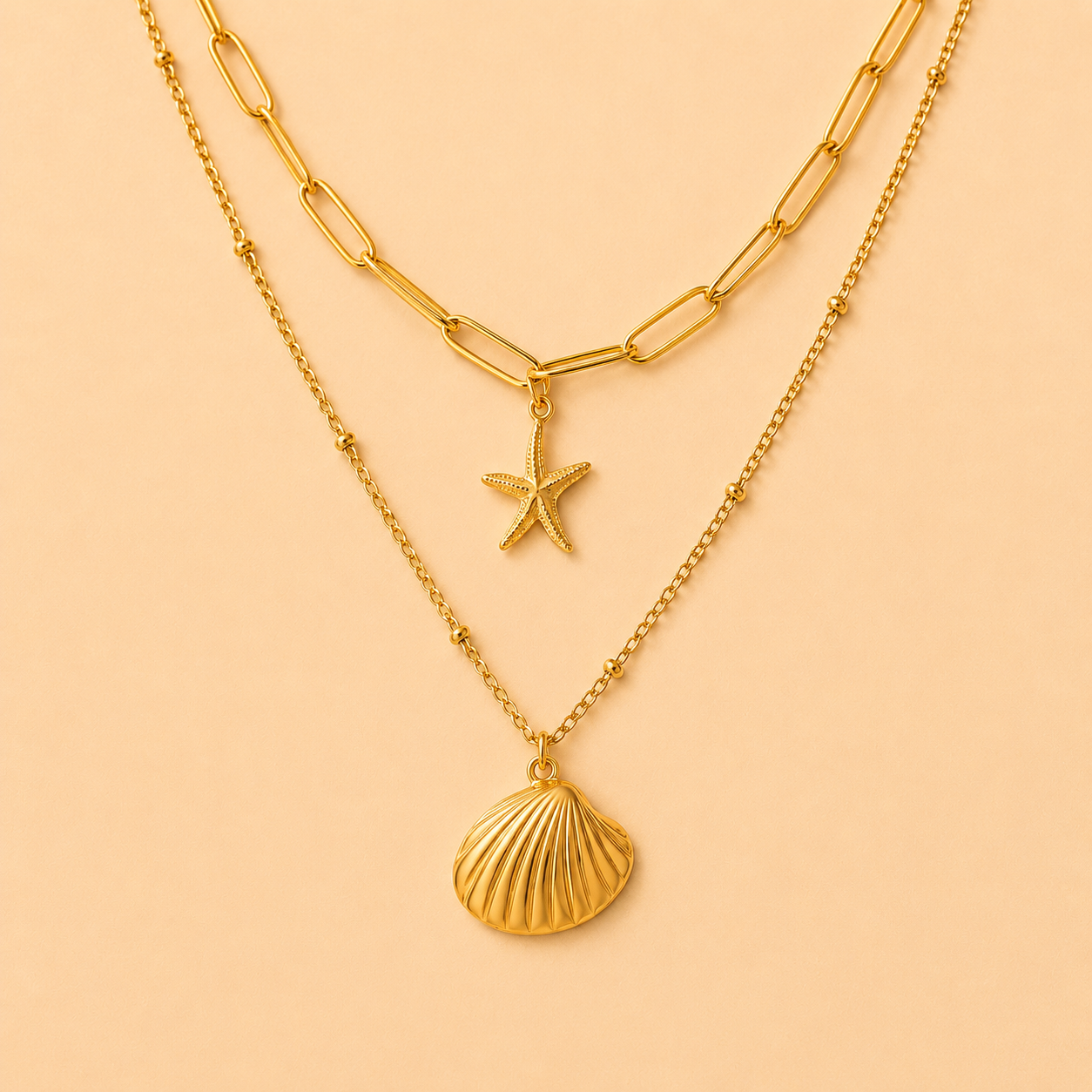 Two gold necklaces with starfish and shell pendants on a peach background