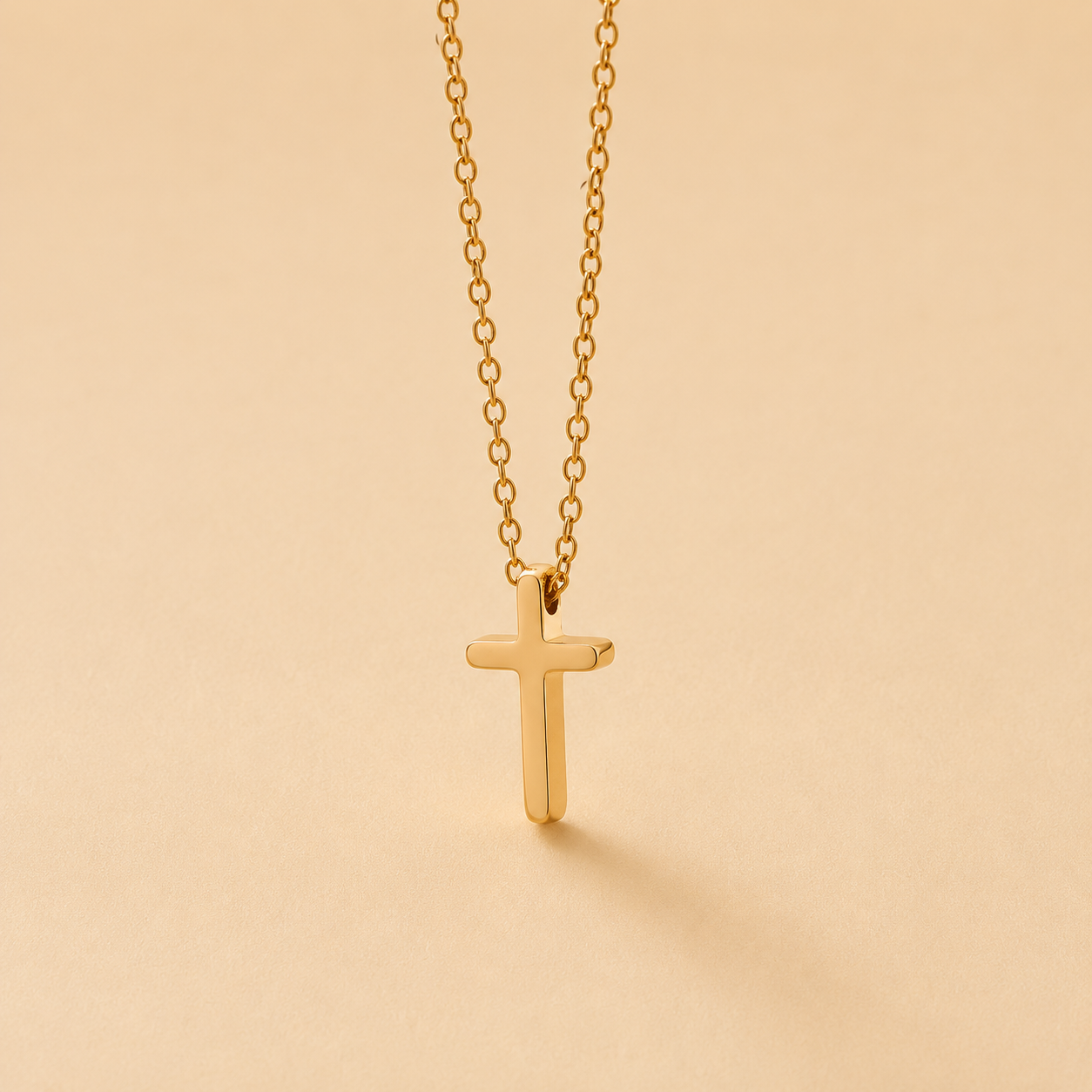 A delicate gold cross pendant necklace hanging from a fine gold chain against a warm beige background.