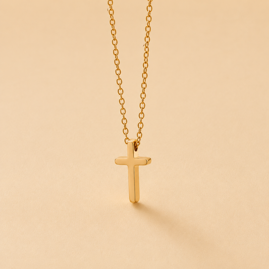 A delicate gold cross pendant necklace hanging from a fine gold chain against a warm beige background.