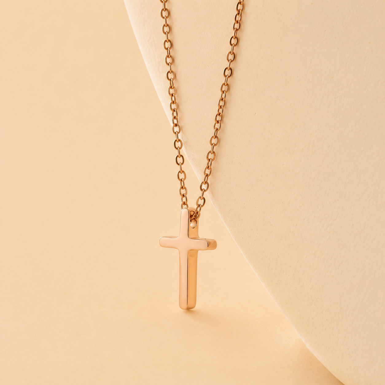 A delicate rose gold cross pendant necklace on a matching fine link chain, displayed on a cream-colored jewelry bust against a warm beige background.