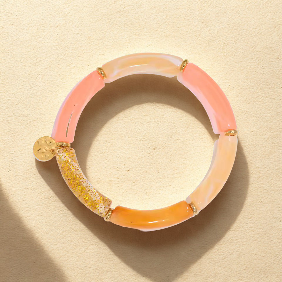 Two-toned pink and orange bracelet with gold accents on a beige background