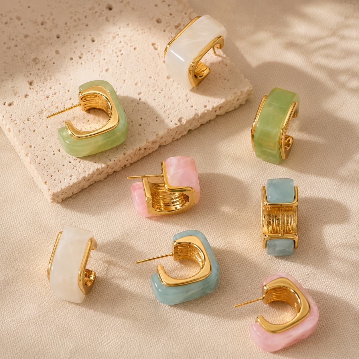 Set of gold and colorful hoop earrings on a textured beige surface