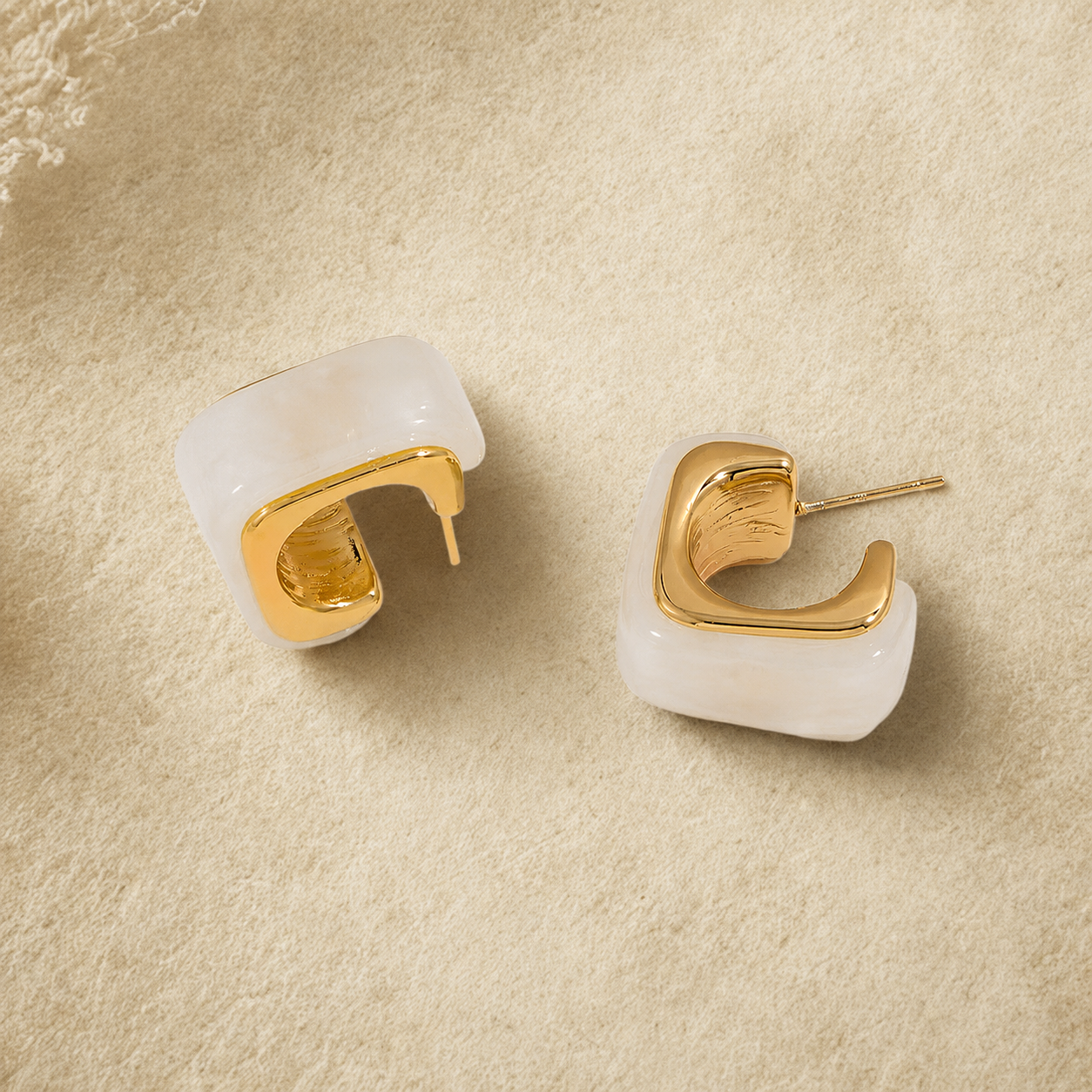 Gold and white hoop earrings on a beige textured surface