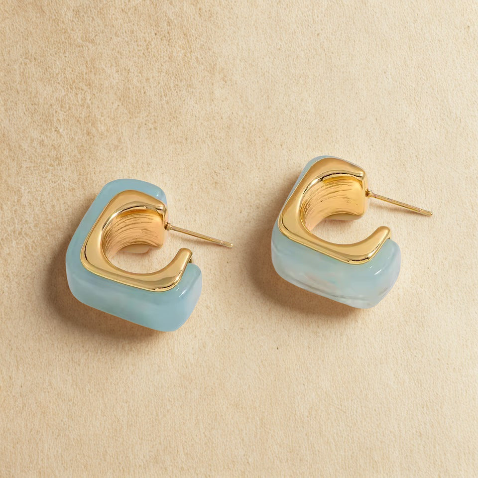 Gold and light blue earrings on a beige background