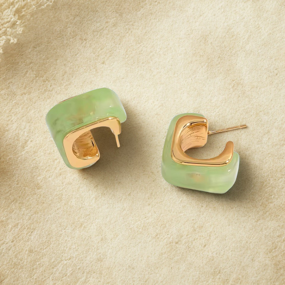 Pair of green hoop earrings with gold accents on a beige surface