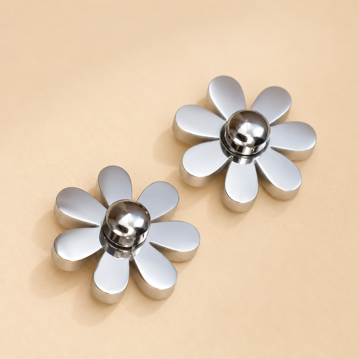 Two metallic flower-shaped decorative knobs with silver petals and polished chrome centers, displayed on a warm beige background.