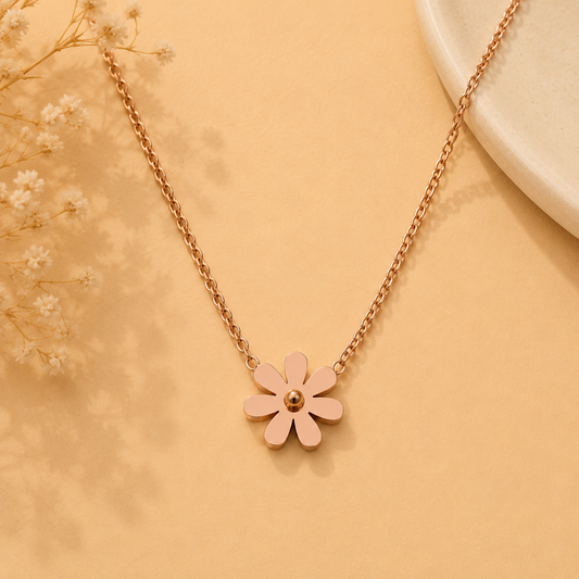 A delicate rose gold chain necklace featuring a small five-petal flower pendant with a gold center, displayed on a warm beige background with dried baby's breath flowers.