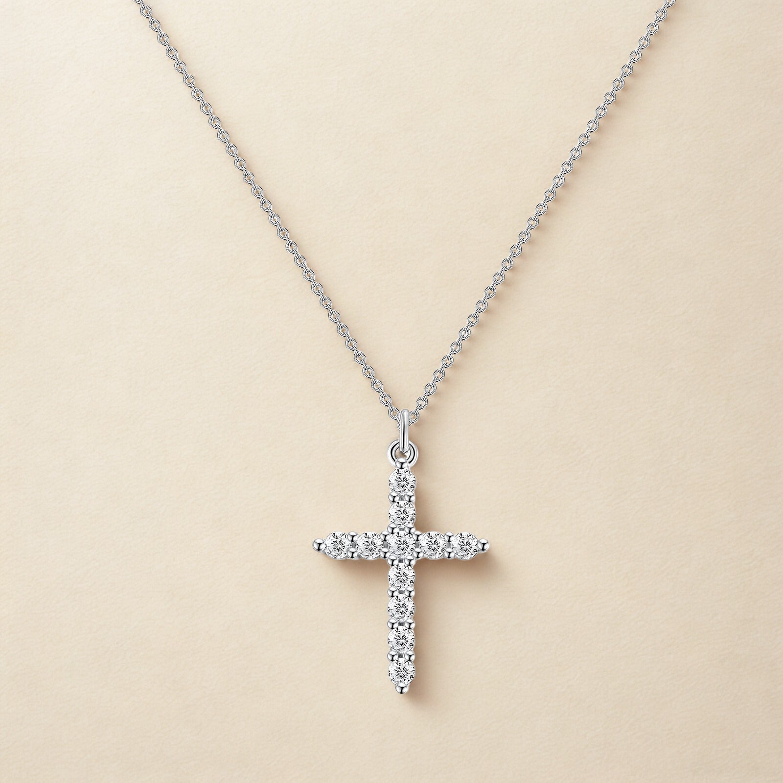 Silver cross pendant necklace on a beige background