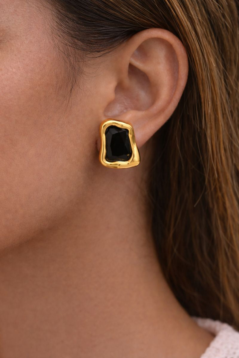Gold earring with a black gemstone worn by a person