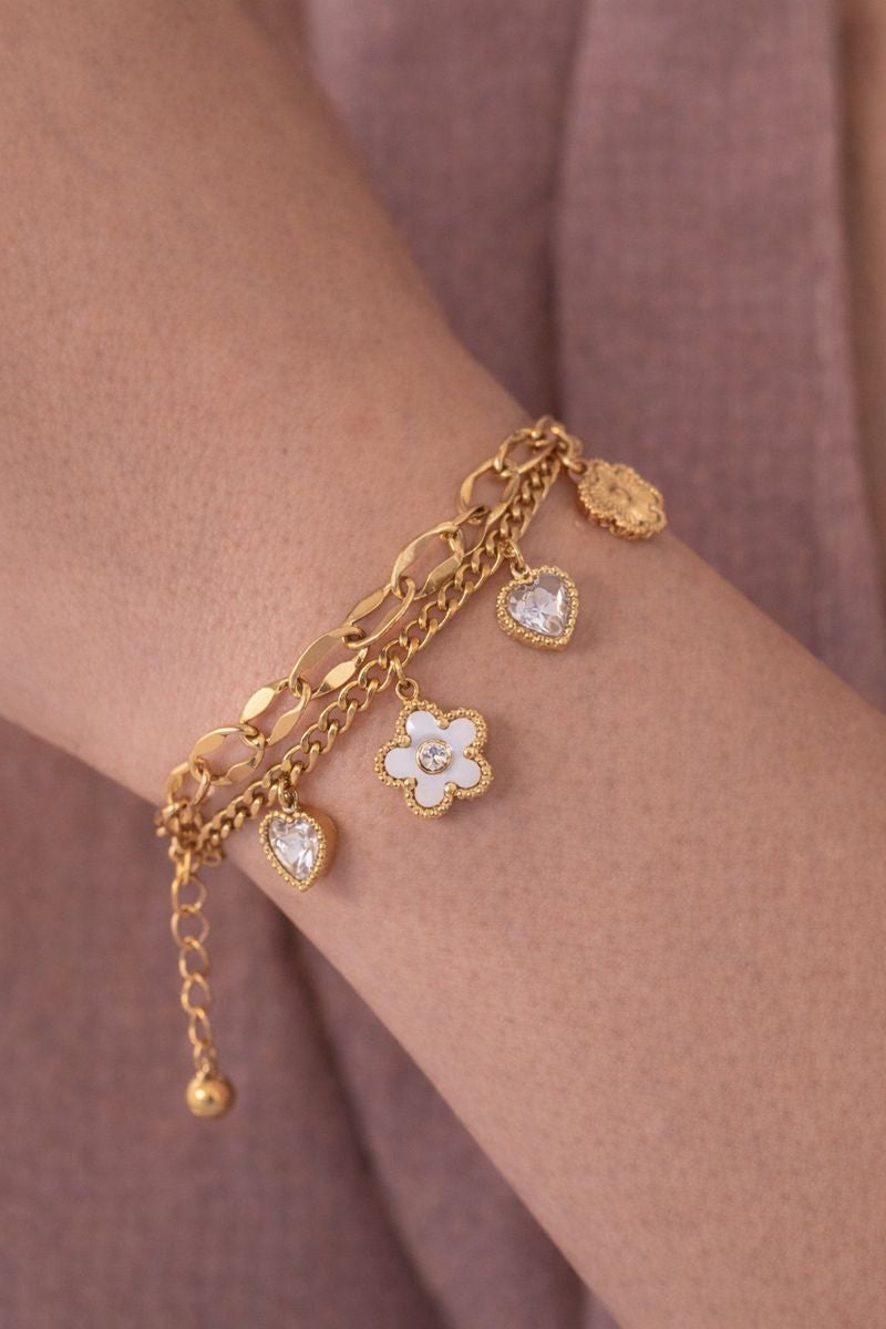 Gold bracelet with floral and heart charms on a wrist against a matching background